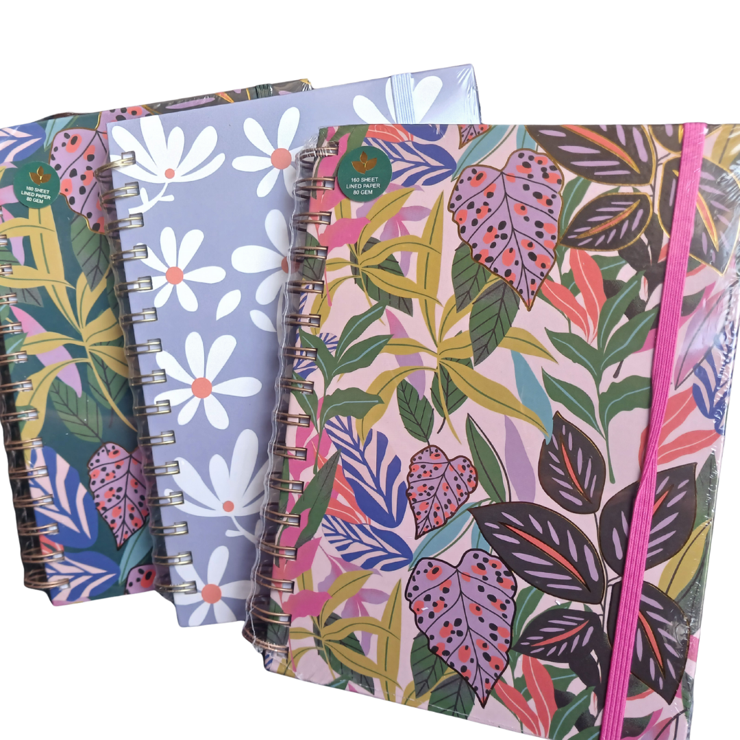 A close-up view of three A5 wire-bound notebooks with assorted vibrant cover prints, including a tropical leaf pattern and a pastel daisy pattern.