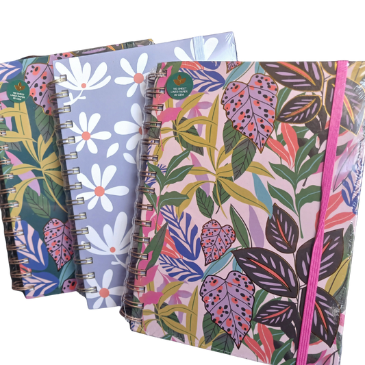 A close-up view of three A5 wire-bound notebooks with assorted vibrant cover prints, including a tropical leaf pattern and a pastel daisy pattern.