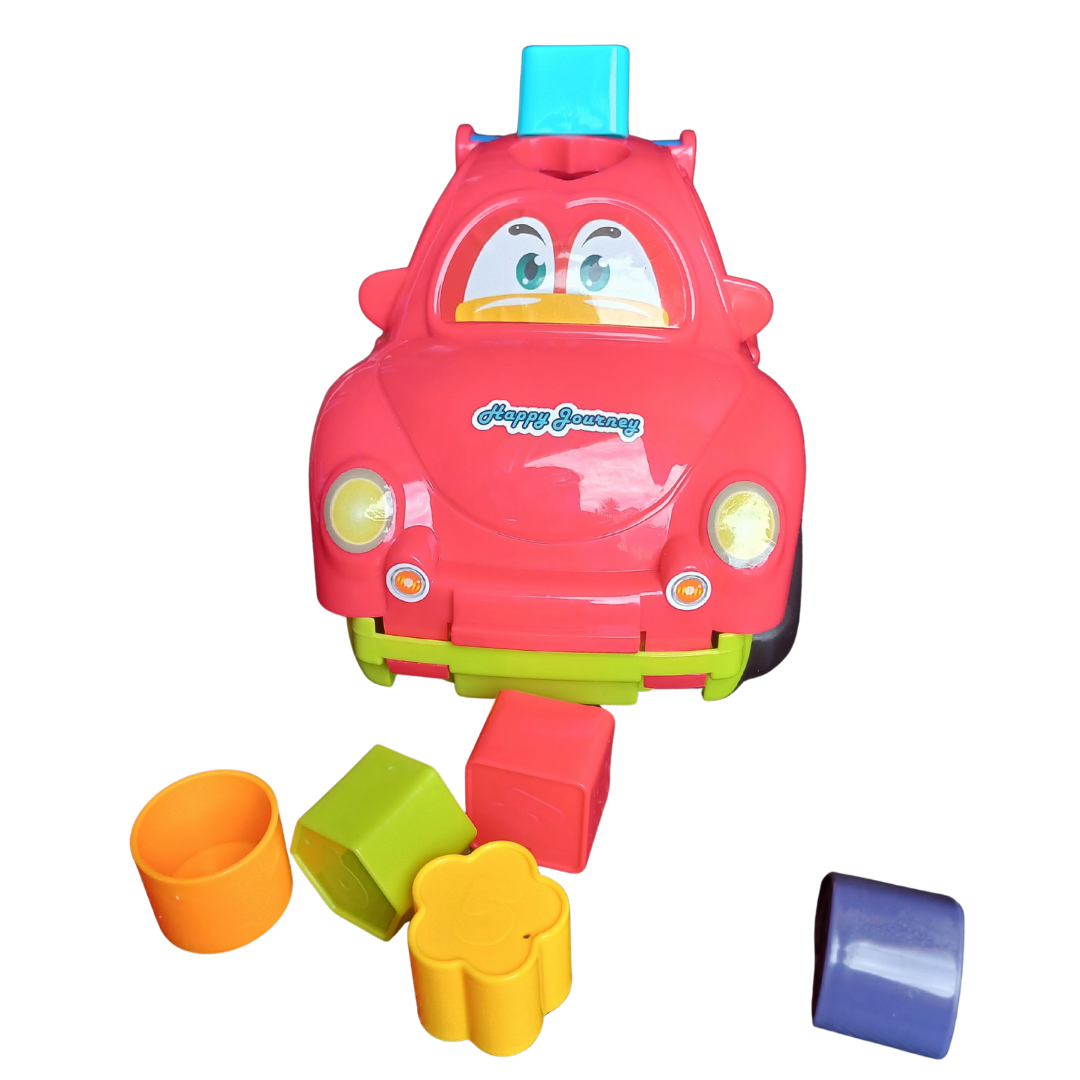A bright red toy car with a "Happy Journey" inscription and blue accent piece, with several colourful sorting blocks (green, orange, yellow, and blue) scattered around the front.