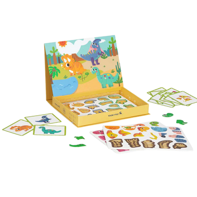 A child playing with the open TookyToy Magnetic Box, which shows a colorful dinosaur scene backdrop and magnetic puzzle pieces on a table.